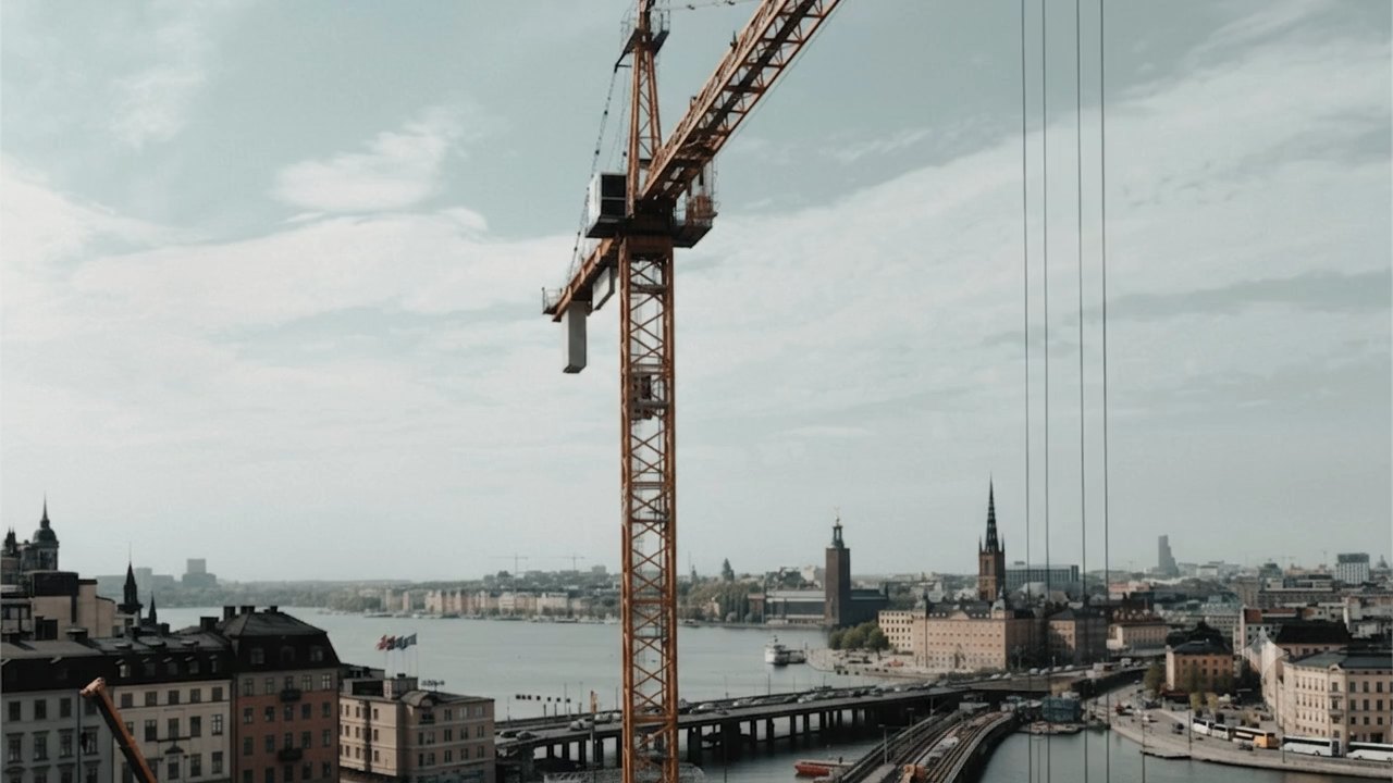 A tower crane standing over a city-centre construction site: excavation and site works below, the city and waterfront behind.